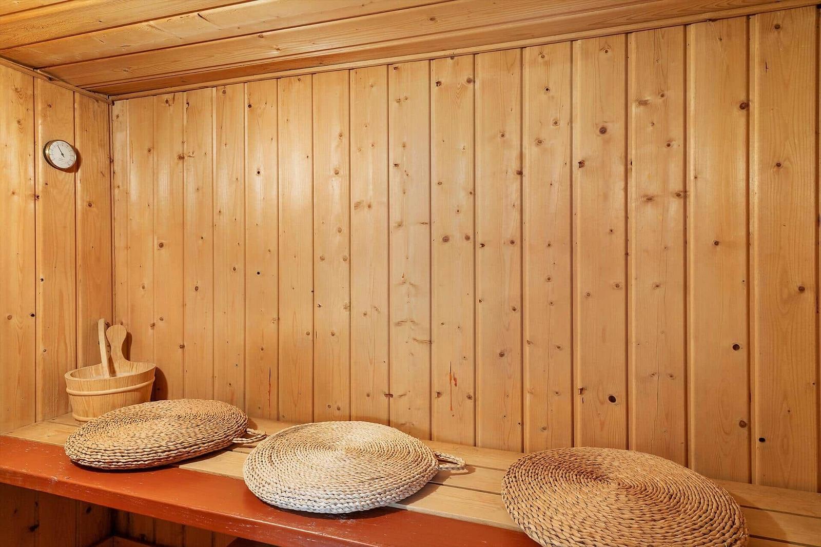 Sauna mit Holzwand, Sitzbank und geflochtenen Kissen.