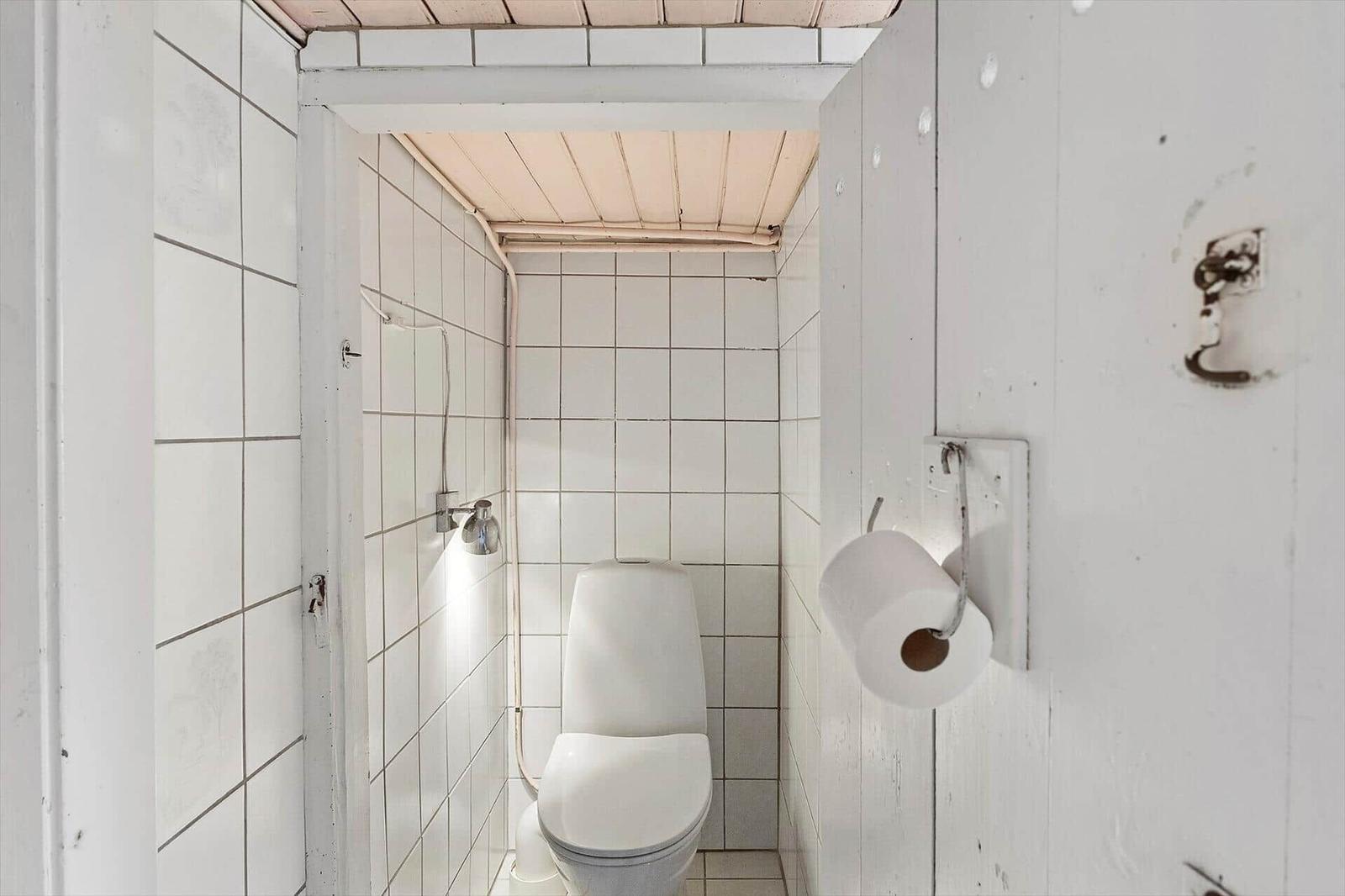 Badezimmer mit Toilette und Dusche, weiße Fliesen und Holzdecke
