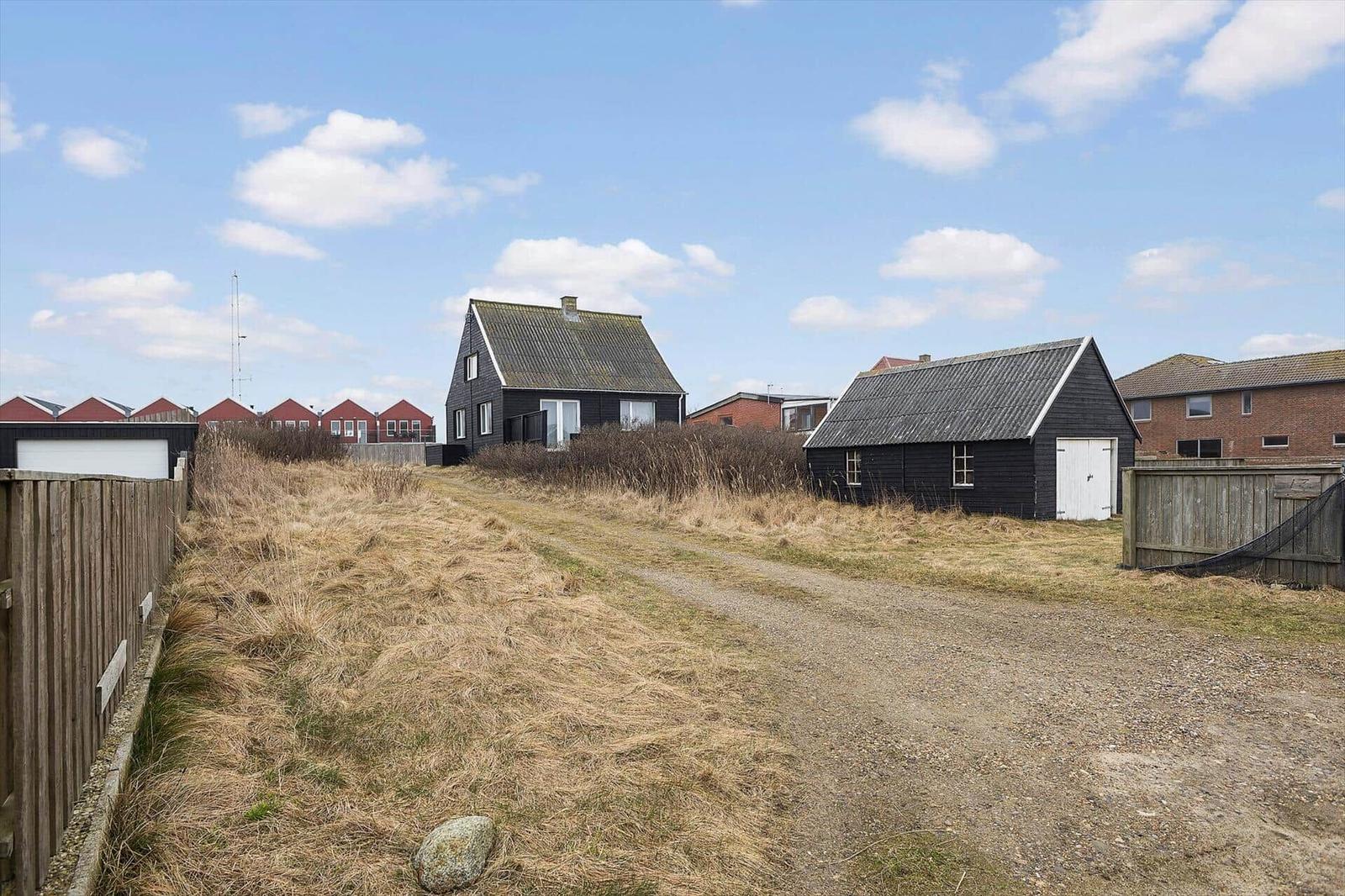Zwei schwarze Häuser mit Schopf und Dach, umgeben von trockenem Gras und einem unbefestigten Weg.