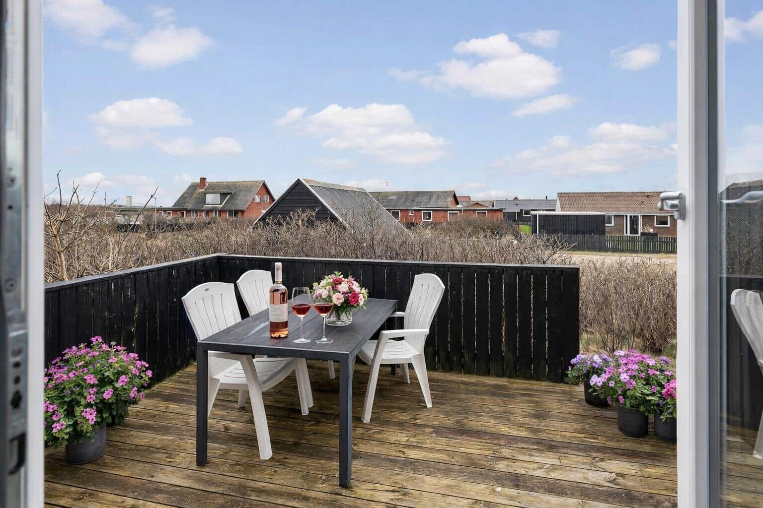Terrasse mit Tisch, Stühlen und Blumen. Blick auf Häuser und Himmel.
