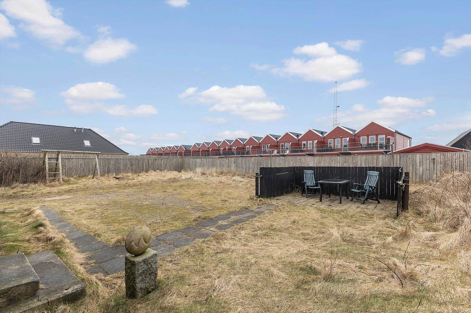 Hinterhof mit Tisch und Stühlen, Holzzaun und roten Häusern im Hintergrund.