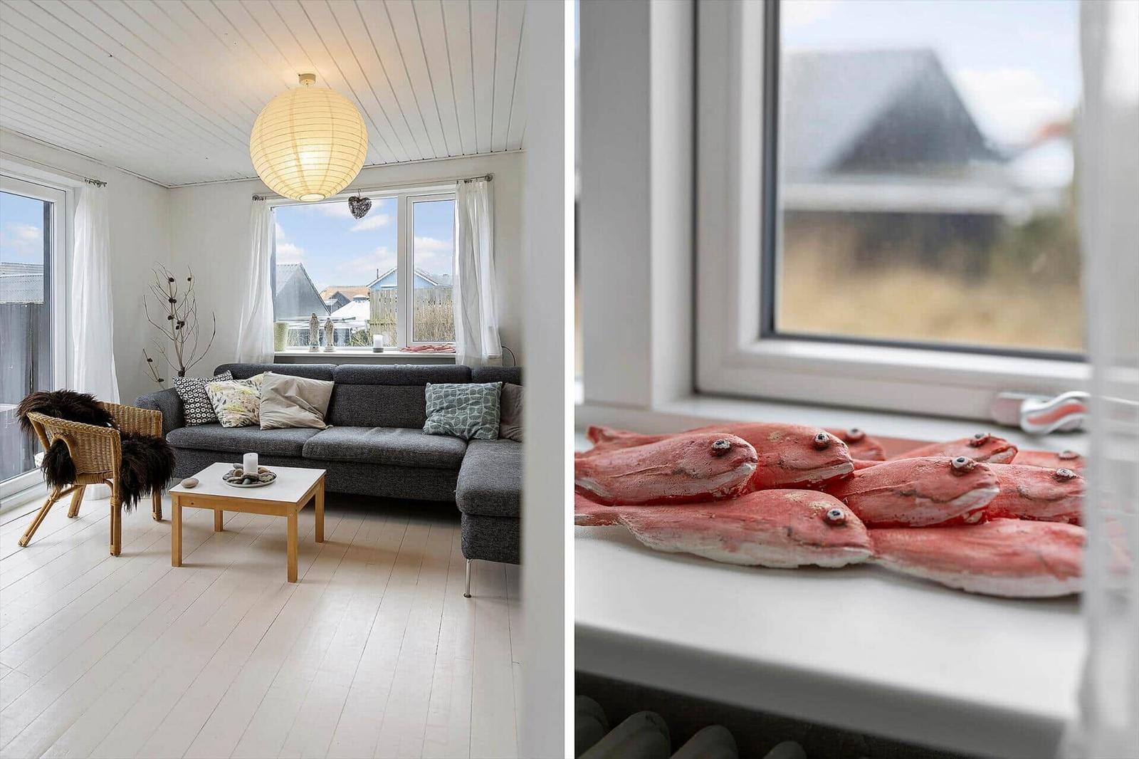 Wohnzimmer mit grauem Sofa und Holztisch. Fensterbank mit roten Fischfiguren.