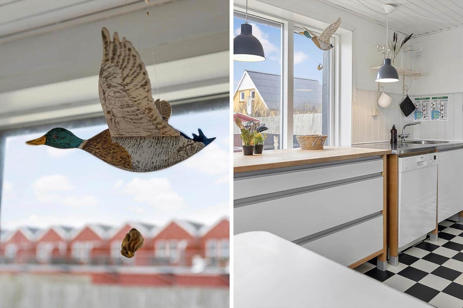 Küche mit Holzoberfläche und schwarz-weißem Fliesenboden. Hängendes Enten-Dekor vor Fenster.