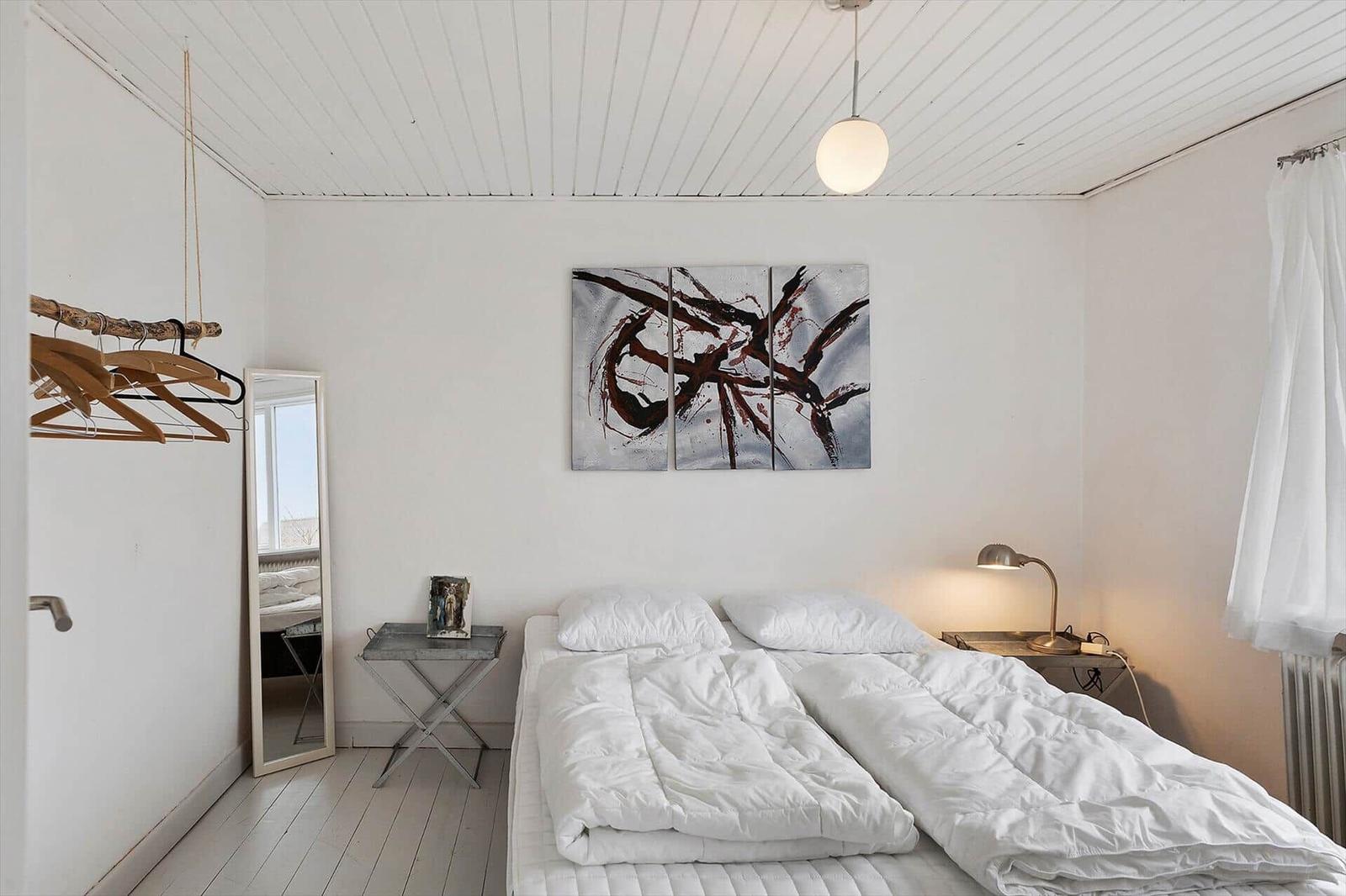 Schlafzimmer mit Bett, Wandbild und Kleiderständer.