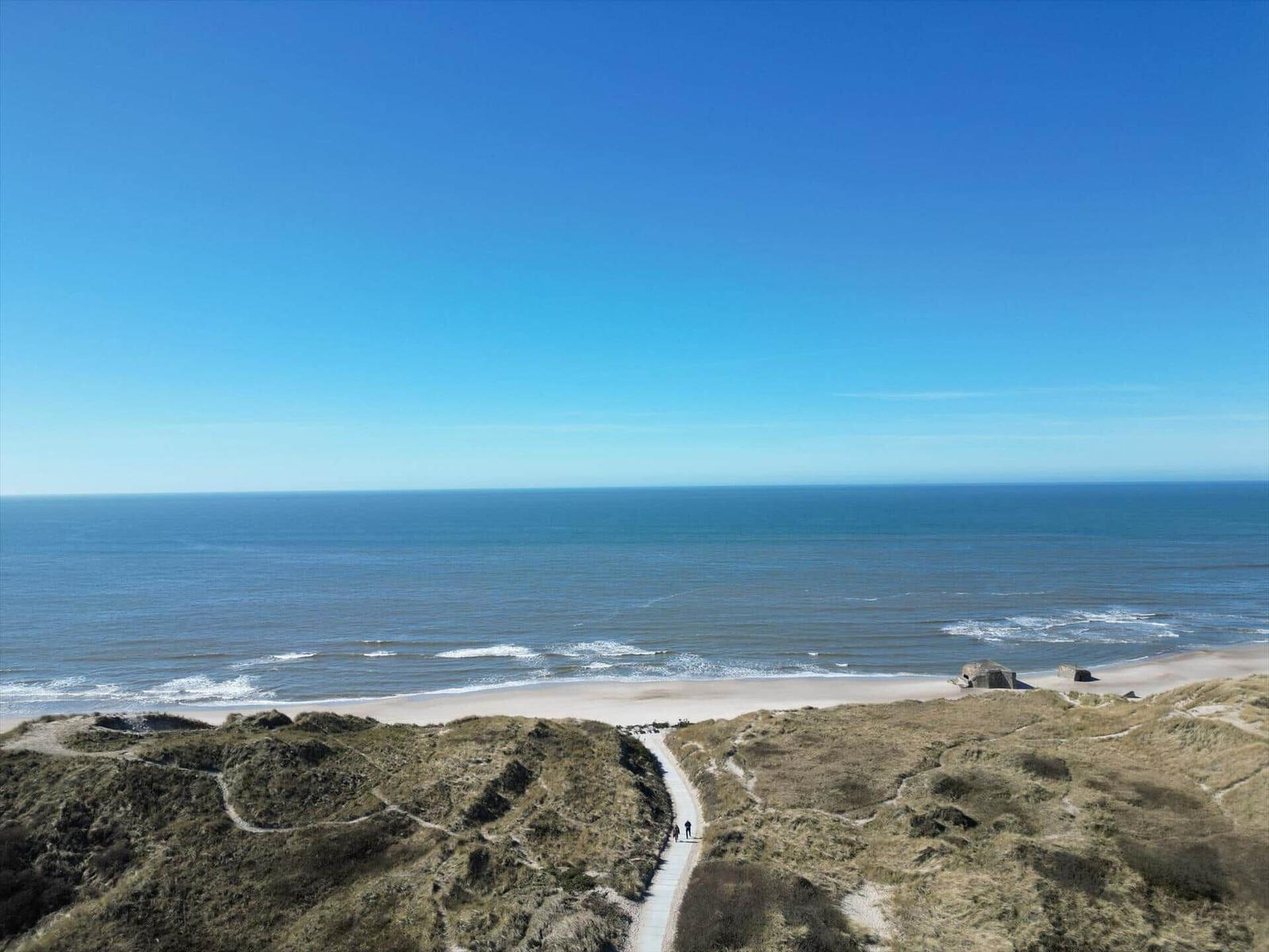 Wanderweg führt von Dünen zu Strand und Meer unter klarem Himmel.