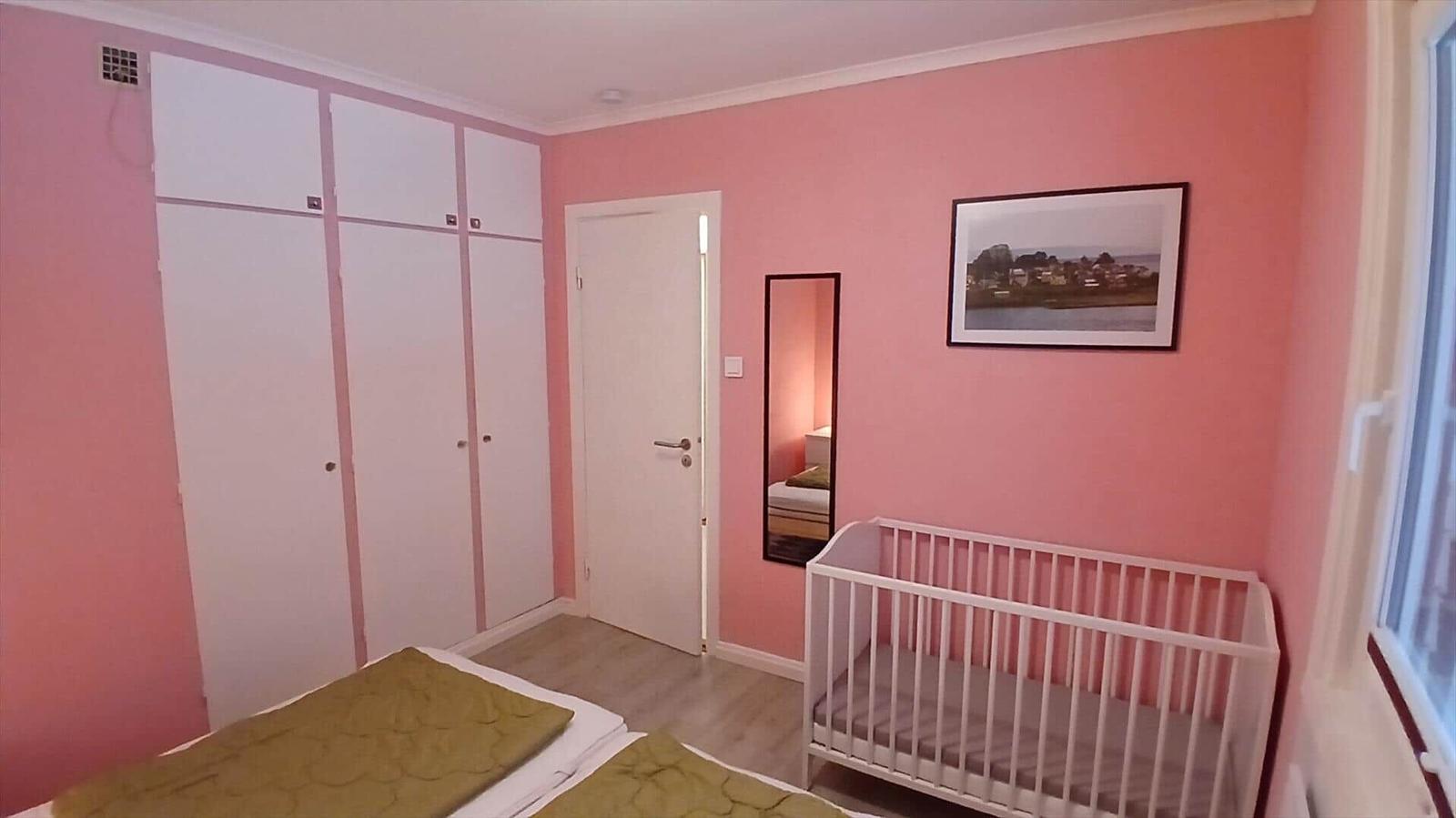 Schlafzimmer mit Babybett, Kleiderschrank und Wandbild.