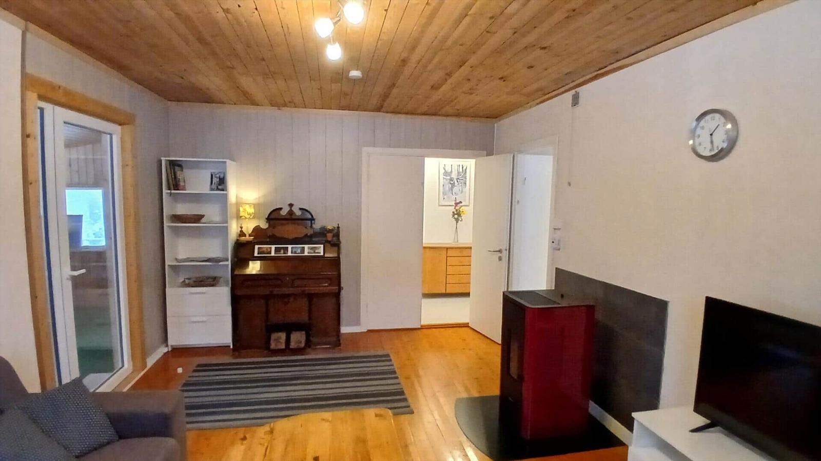 Wohnraum mit Holzboden, Kaminofen und TV. Durchgang zu Schlafzimmer und Küche.