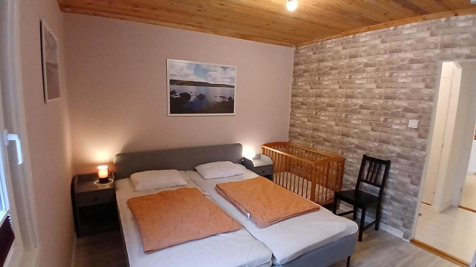 Zimmer mit Doppelbett, Kinderbett und Holzdecke.