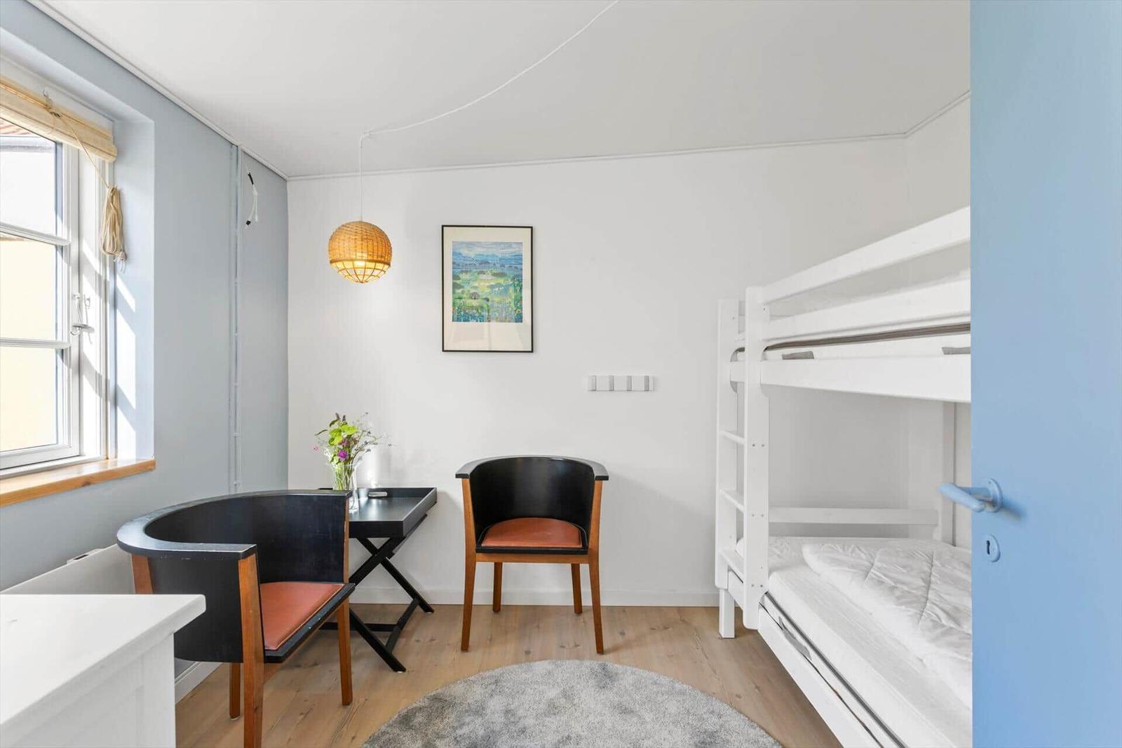 A room with bunk bed, desk and chairs. A picture hangs on the wall.