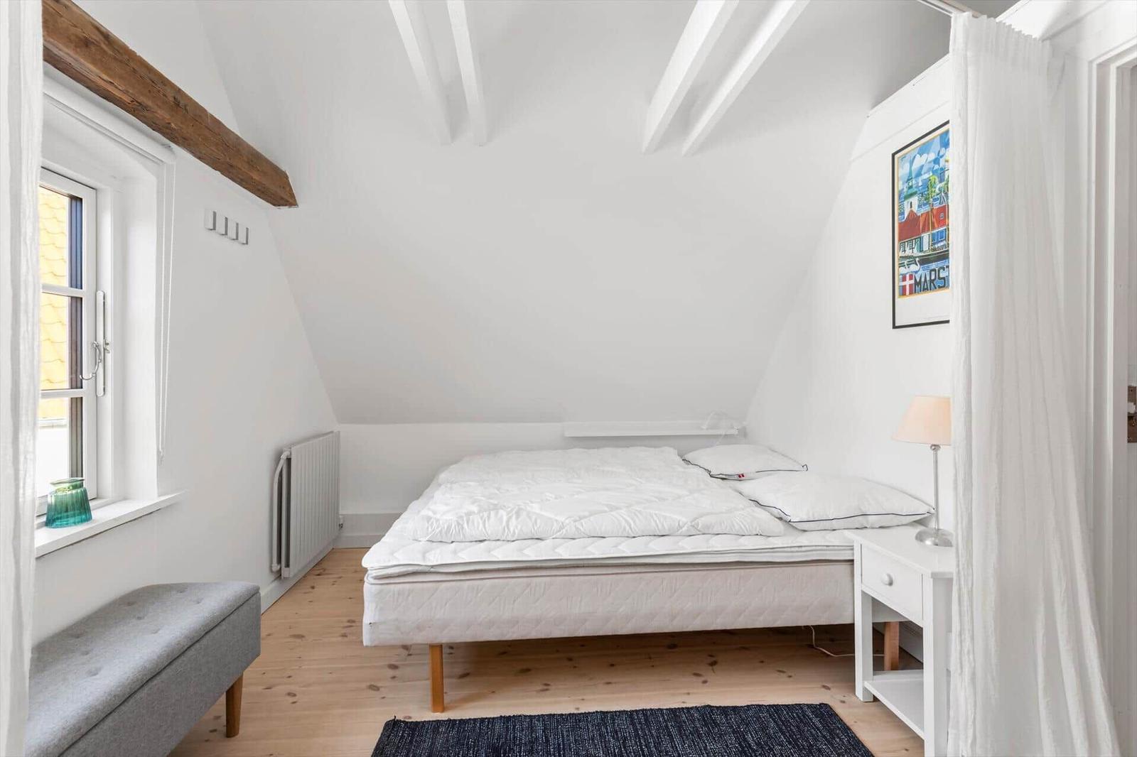 Bedroom with sloped ceiling, white mattress, and wooden floor.