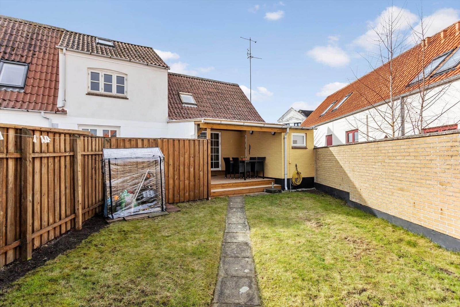 Backyard with terrace, barbecue area, and garden shed. Wooden fence and brick wall surround the space.