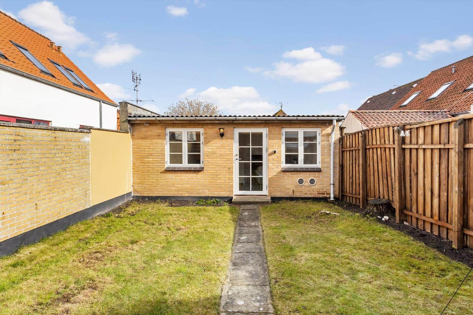 A small house with yellow brick, white door and windows. Yard with lawn and stone path.