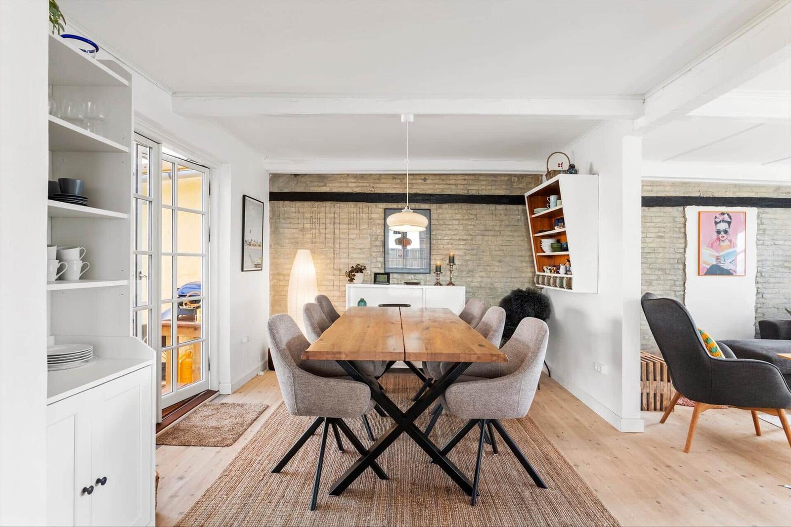 Dining room with wooden table, chairs, and living area in background.