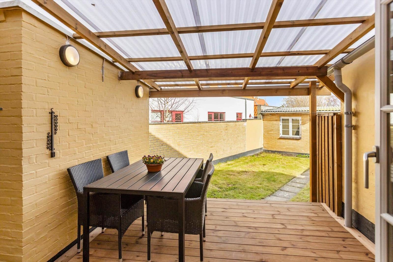 Terrace with table, chairs, and cover. Backyard with lawn and wall.