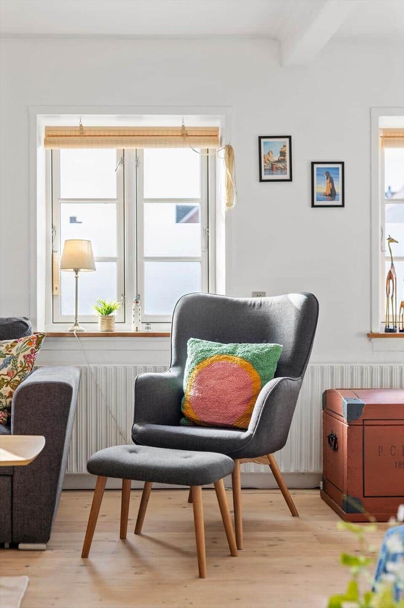 A gray chair with a cushion stands by a window. Next to it is a sofa and a trunk.