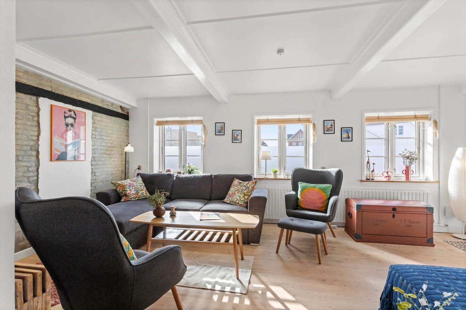 Living room with sofa, two chairs, wooden table, and windows.
