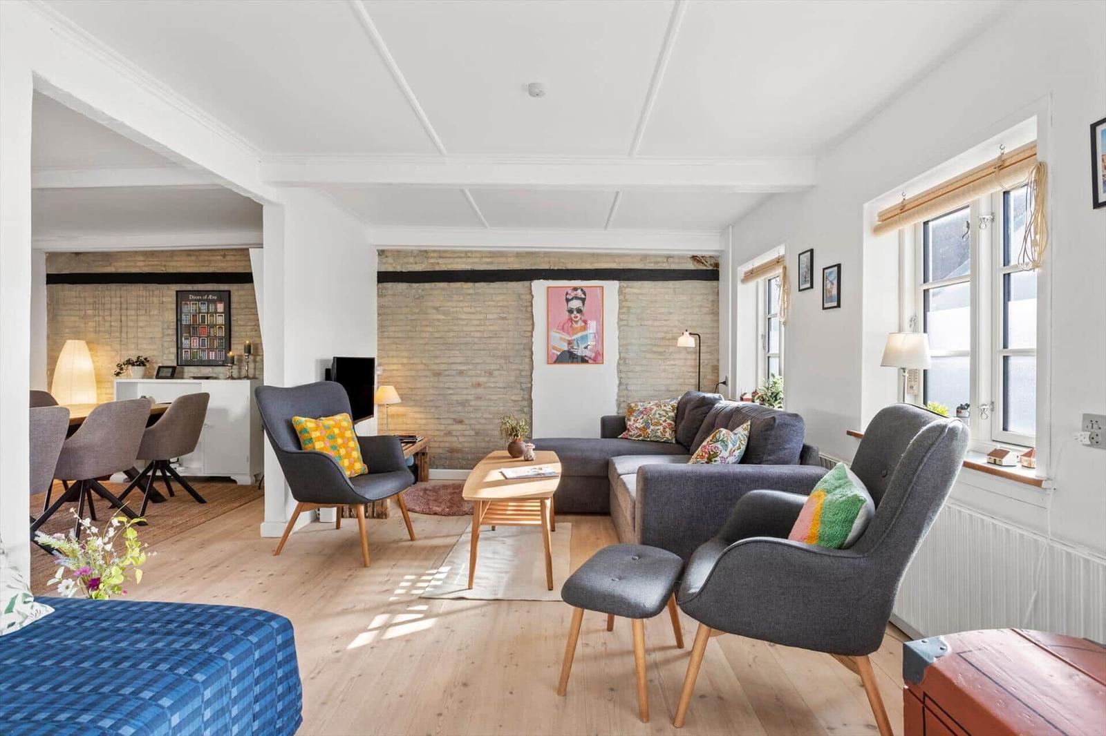 Living room with sofa, two chairs, and wooden floor. Connected dining area with table and chairs.