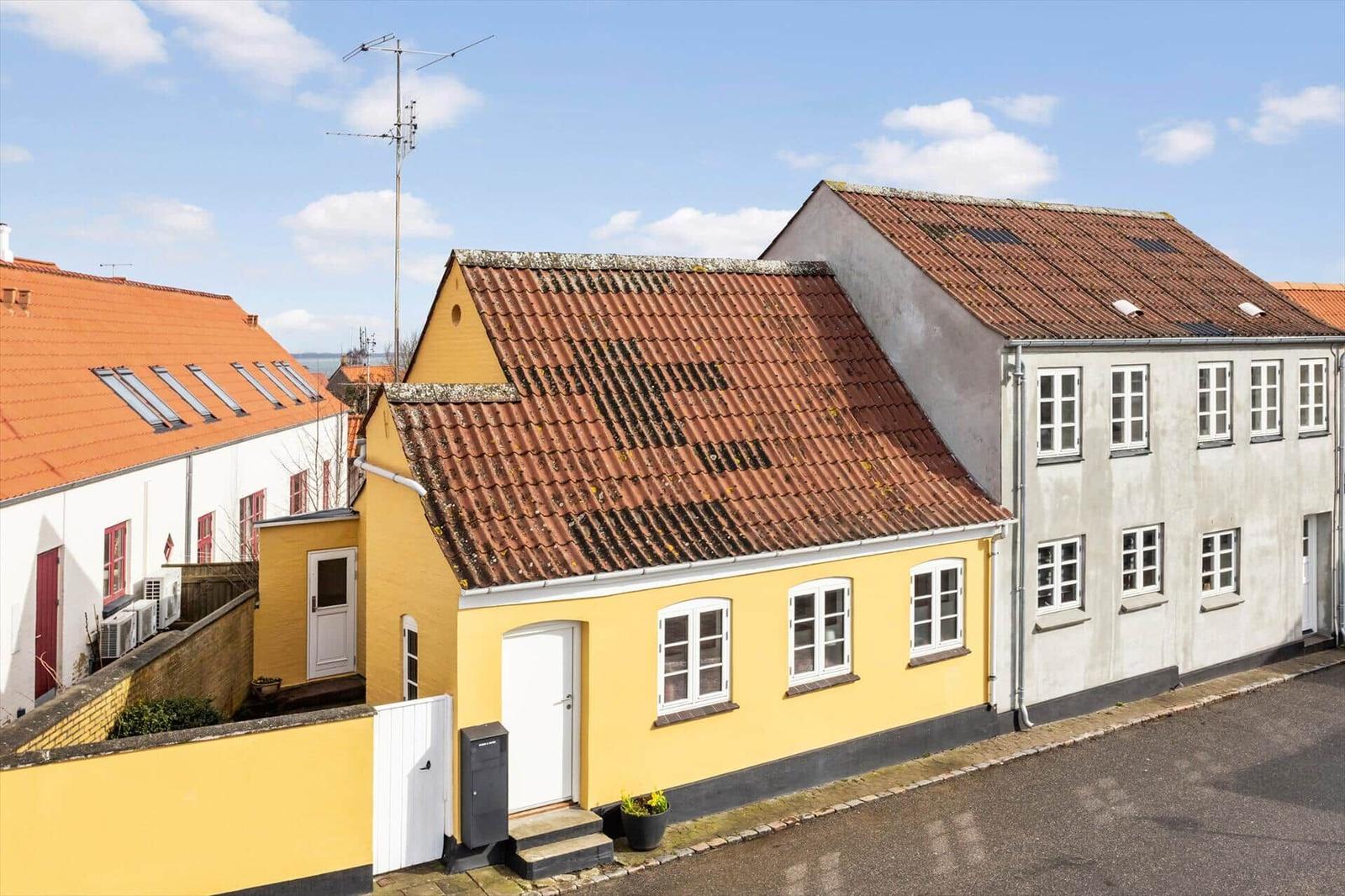 Yellow house with red roof and white windows on a street.