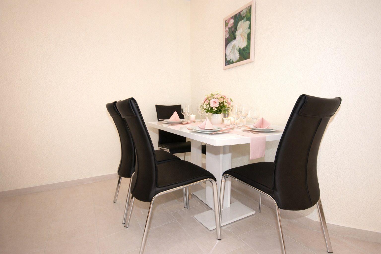 Esszimmer mit weißem Tisch, schwarzen Stühlen und Blumendekoration an der Wand.