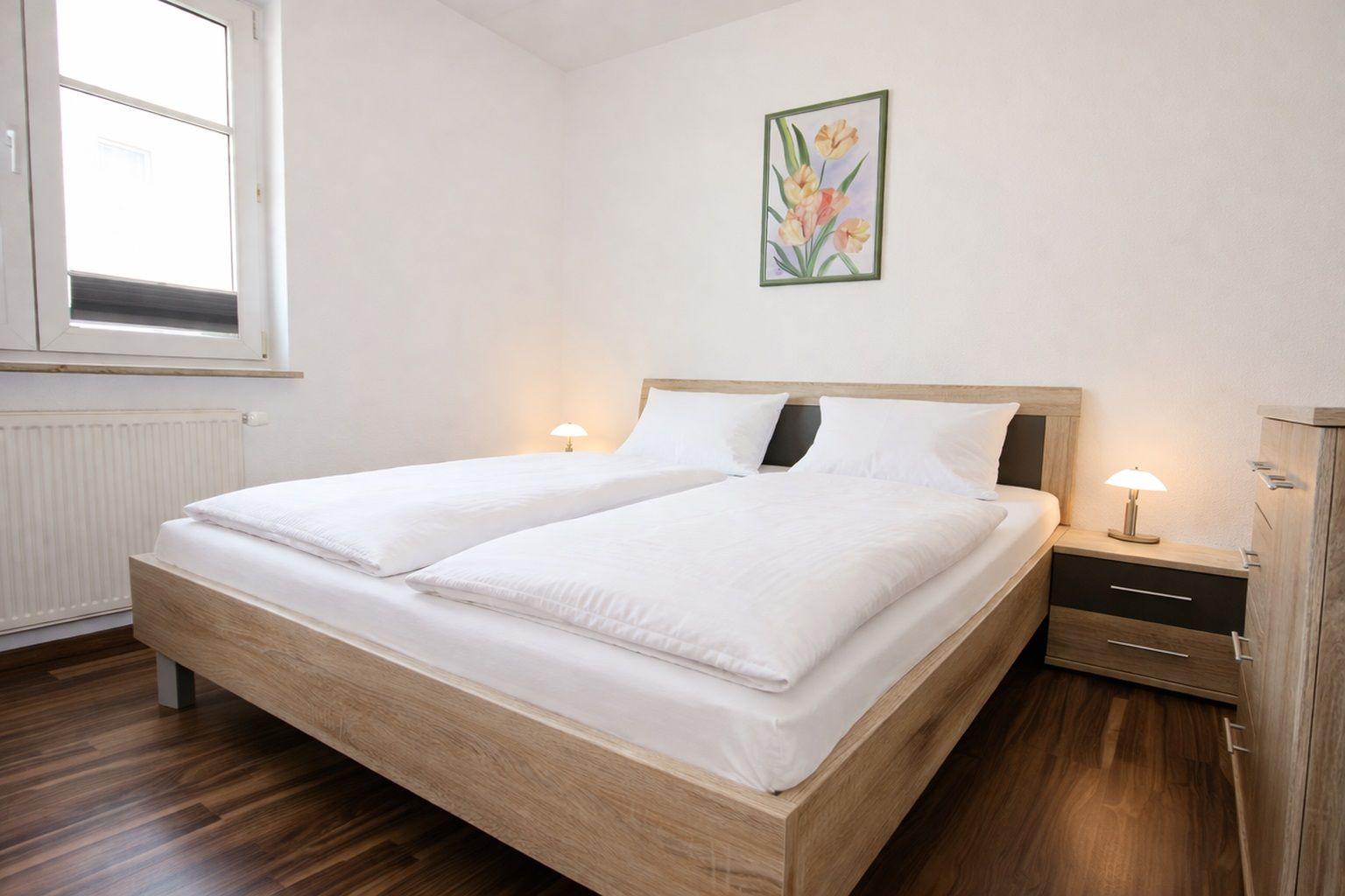 Schlafzimmer mit Doppelbett, Nachttisch und Fenster. Holzboden und Wandbild mit Tulpen.