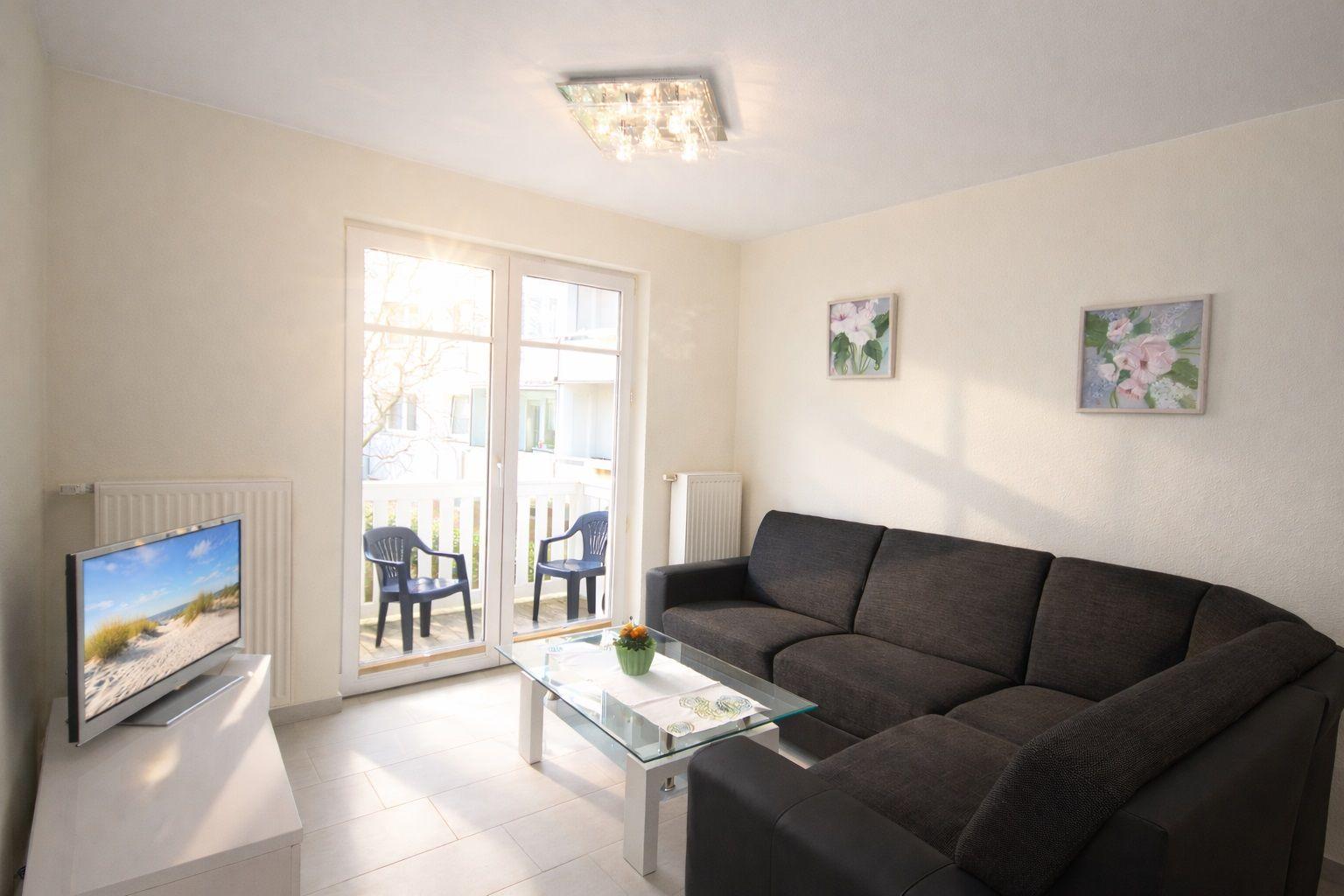 Wohnzimmer mit Sofa, Glas-Tisch und Balkon. Fernseher auf weißen Möbeln.