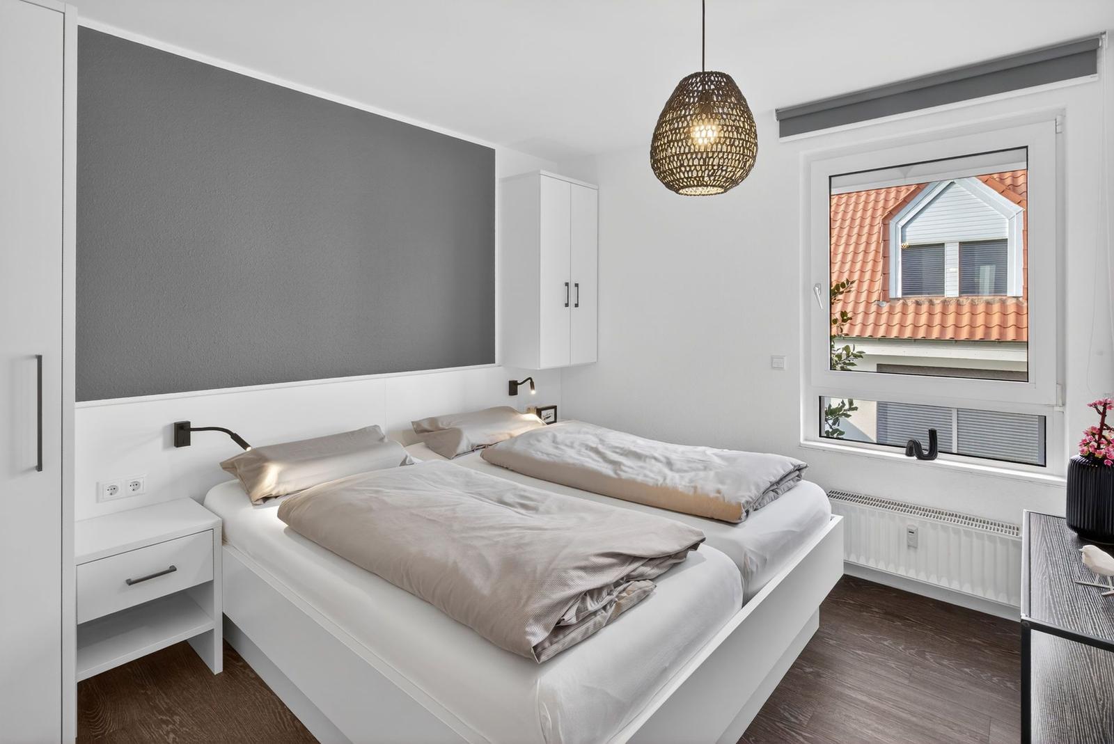Schlafzimmer mit Doppelbett, Fenster und Deckenleuchte.