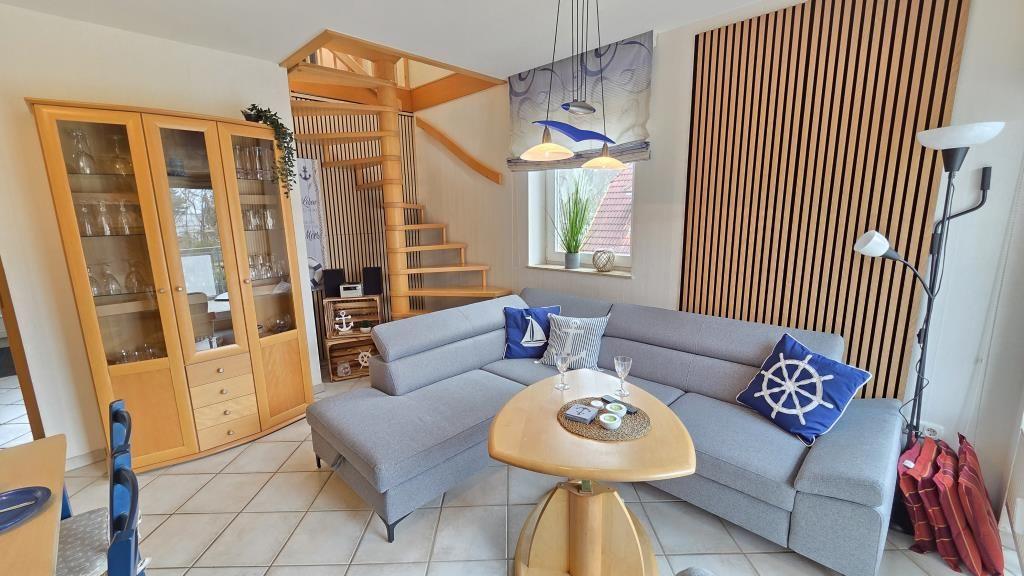 Wohnzimmer mit Sofa, Tisch und Glaswand. Holztreppe und Fenster mit Pflanze.