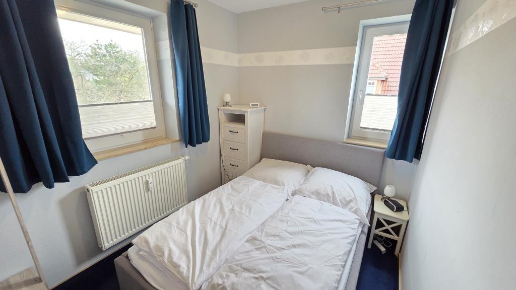 Schlafzimmer mit Doppelbett, zwei Fenstern und Schrank.