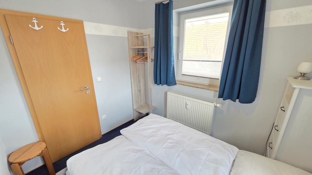 Schlafzimmer mit Bett, Kleiderständer und Fenster mit blauen Vorhängen.