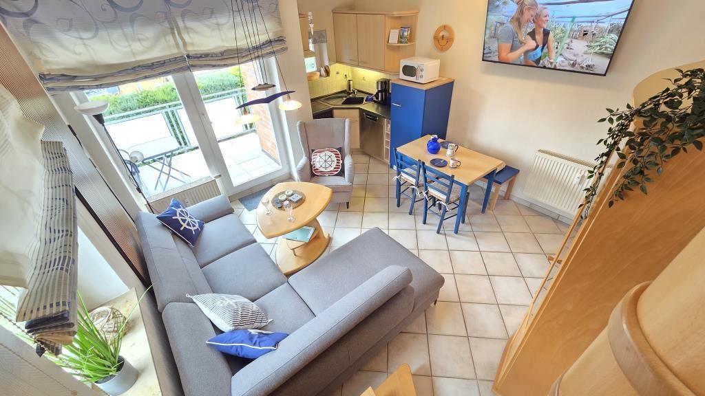 Wohnbereich mit Sofa, Esstisch und Küchenzeile. Balkon mit Sicht auf Grün.