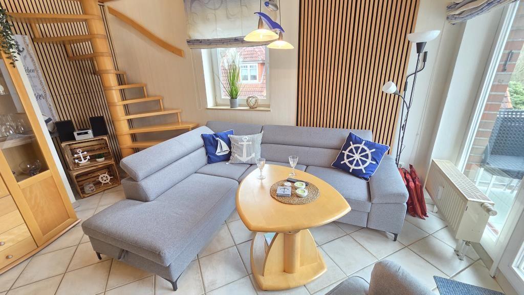 Wohnzimmer mit grauem Sofa, Holztisch und Treppenhaus.