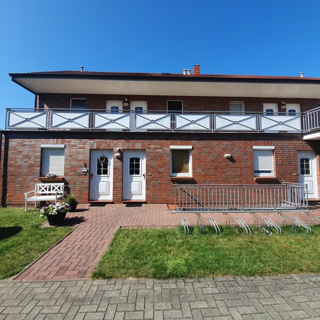 Zweistöckiges Haus mit Balkon, weißen Türen und gepflastertem Hof.