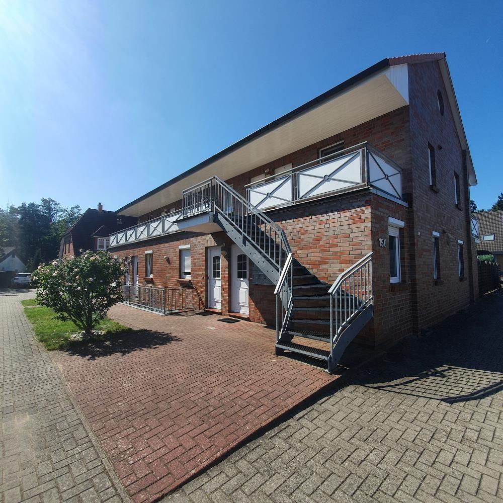 Zweistöckiges Haus mit Außentreppe und Balkon. Vorhof mit Pflanzen und gepflastertem Boden.