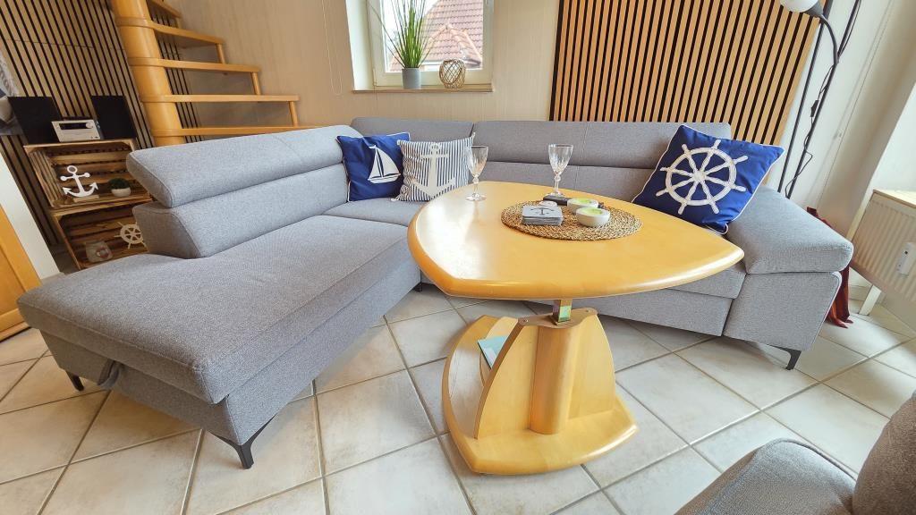 Ein Wohnzimmer mit grauem Sofa, runden Tisch und maritimen Kissen.