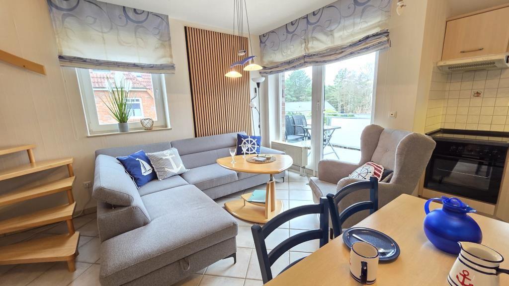 Wohnzimmer mit Sofa, Esstisch und Küchenbereich. Durchgang zur Terrasse mit Sitzgelegenheit.