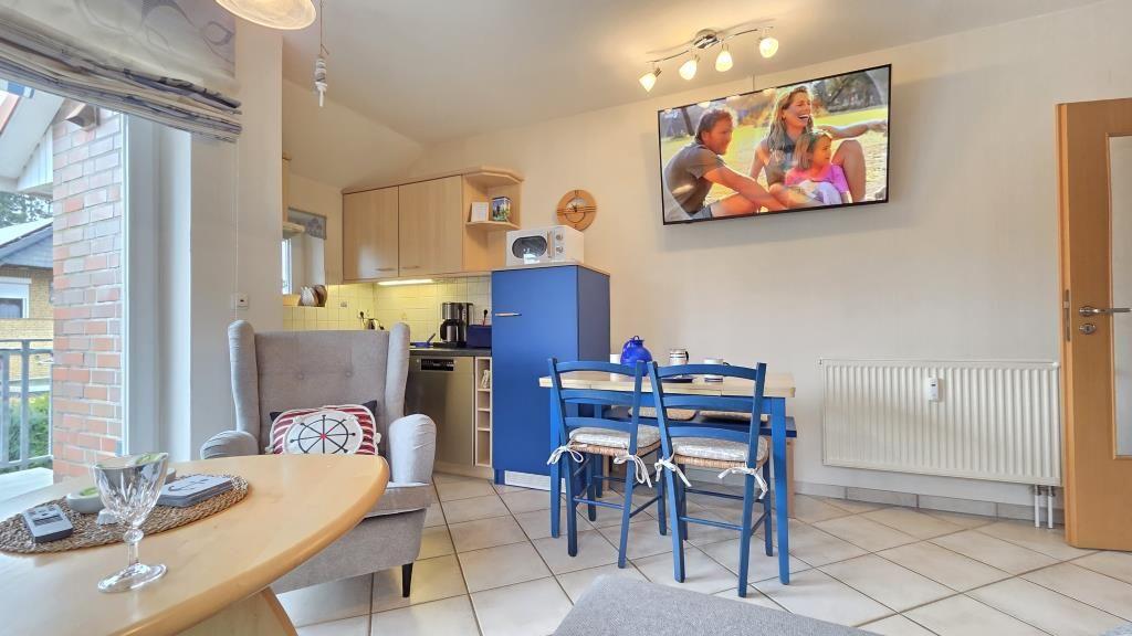 Wohnküche mit TV, Esstisch und Sitzgelegenheit. Blauer Kühlschrank und Fenster zur Terrasse.