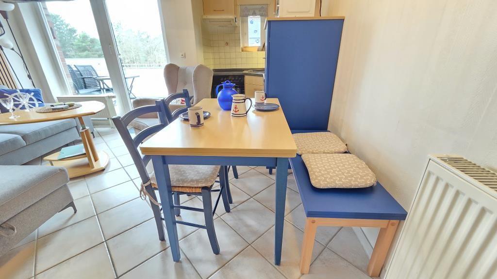 Essbereich mit Tisch, Stühlen und Hocker. Küche und Wohnbereich im Hintergrund.