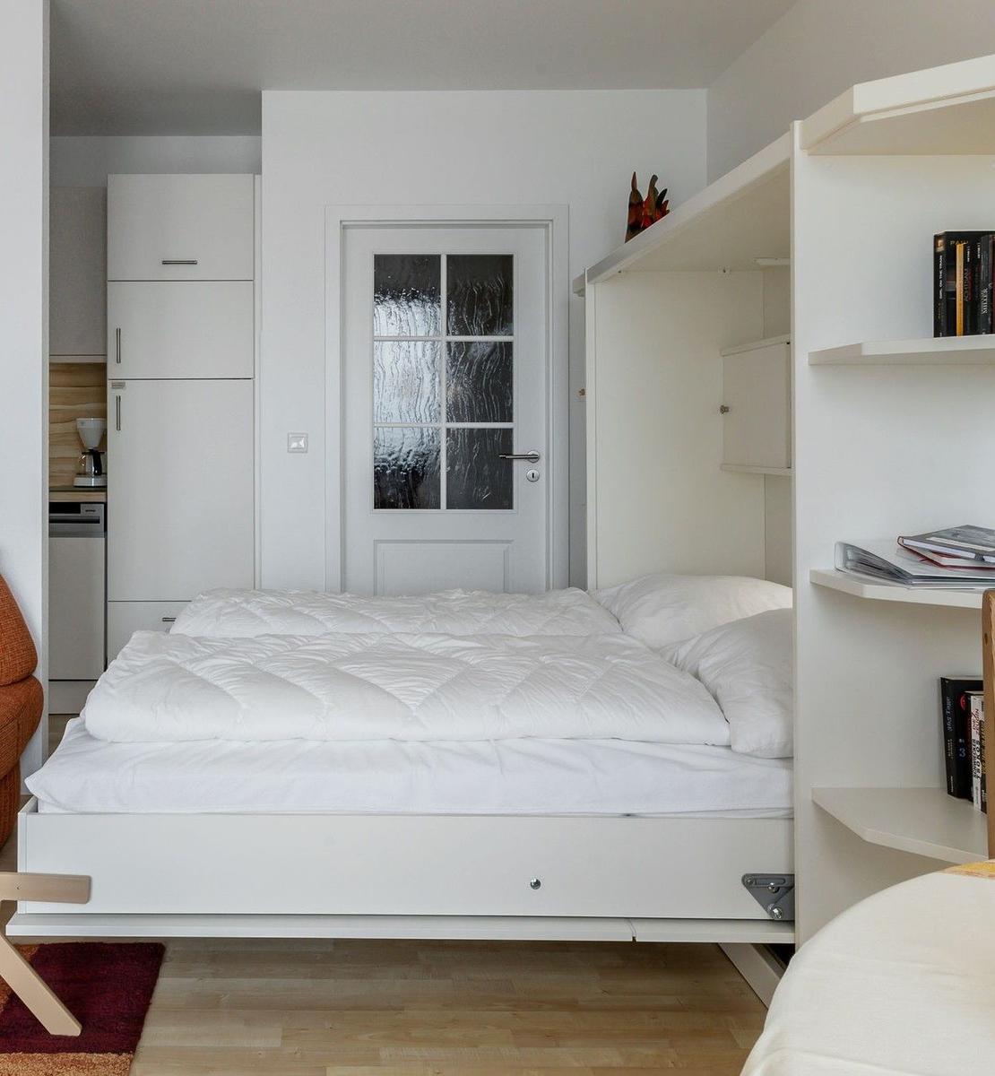 Schlafzimmer mit weißem Bett, Regal und Tür im Hintergrund.