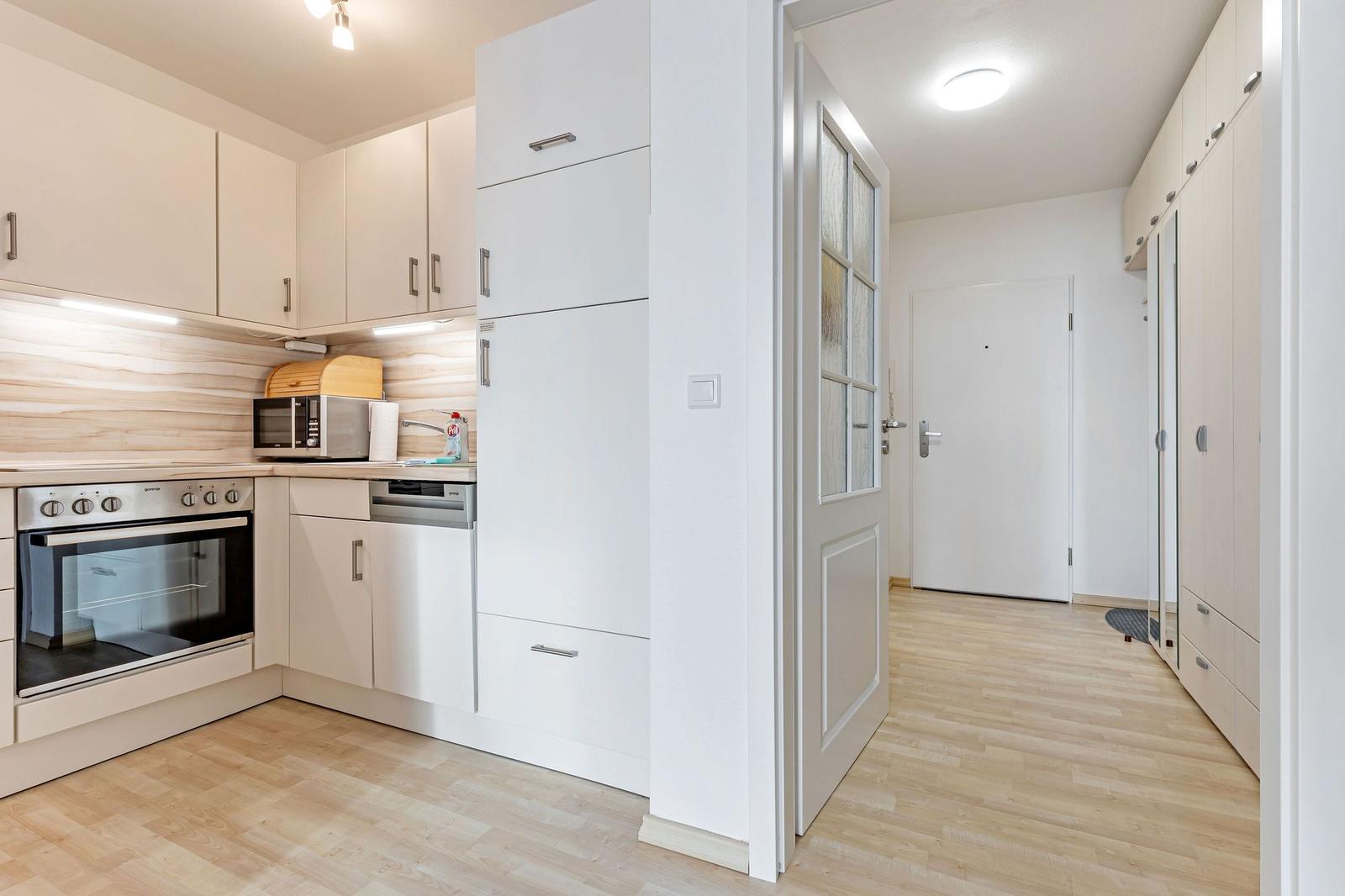 Küche mit integriertem Backofen und Mikrowelle. Flur mit Schrank und Tür.