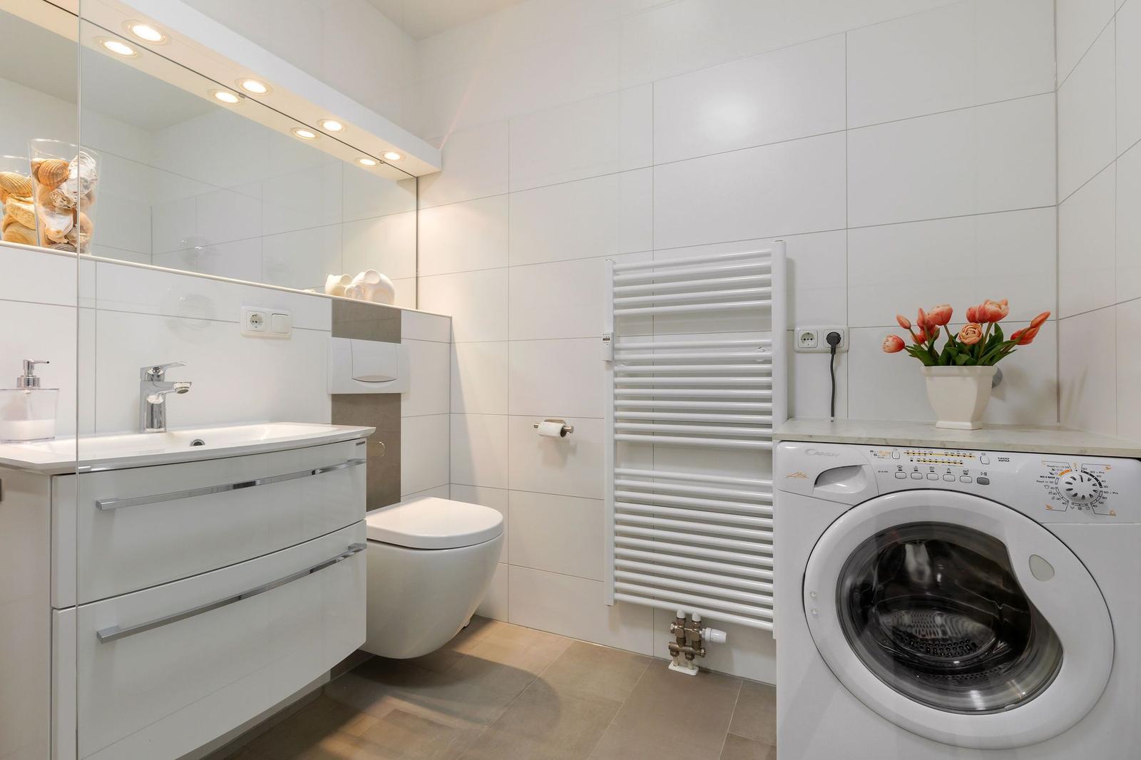 Badezimmer mit Waschmaschine, Spiegel und Heizkörper.