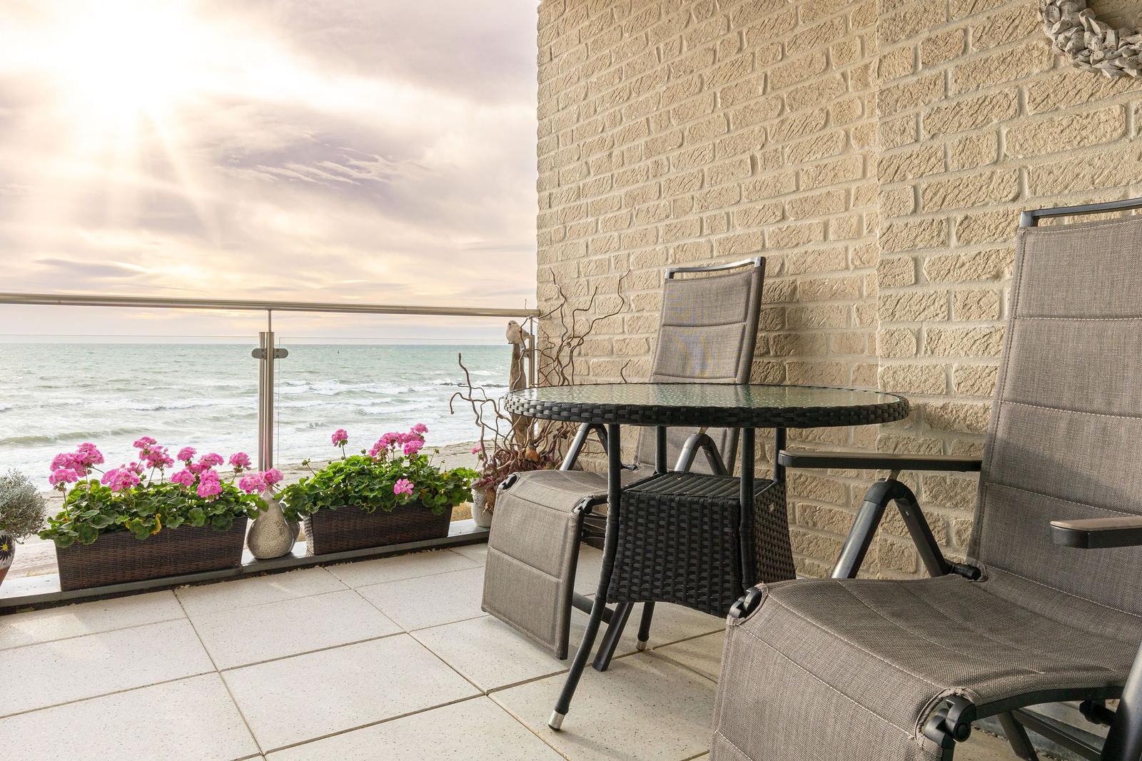 Terrasse mit Sitzgruppe, Blumen und Meerblick.