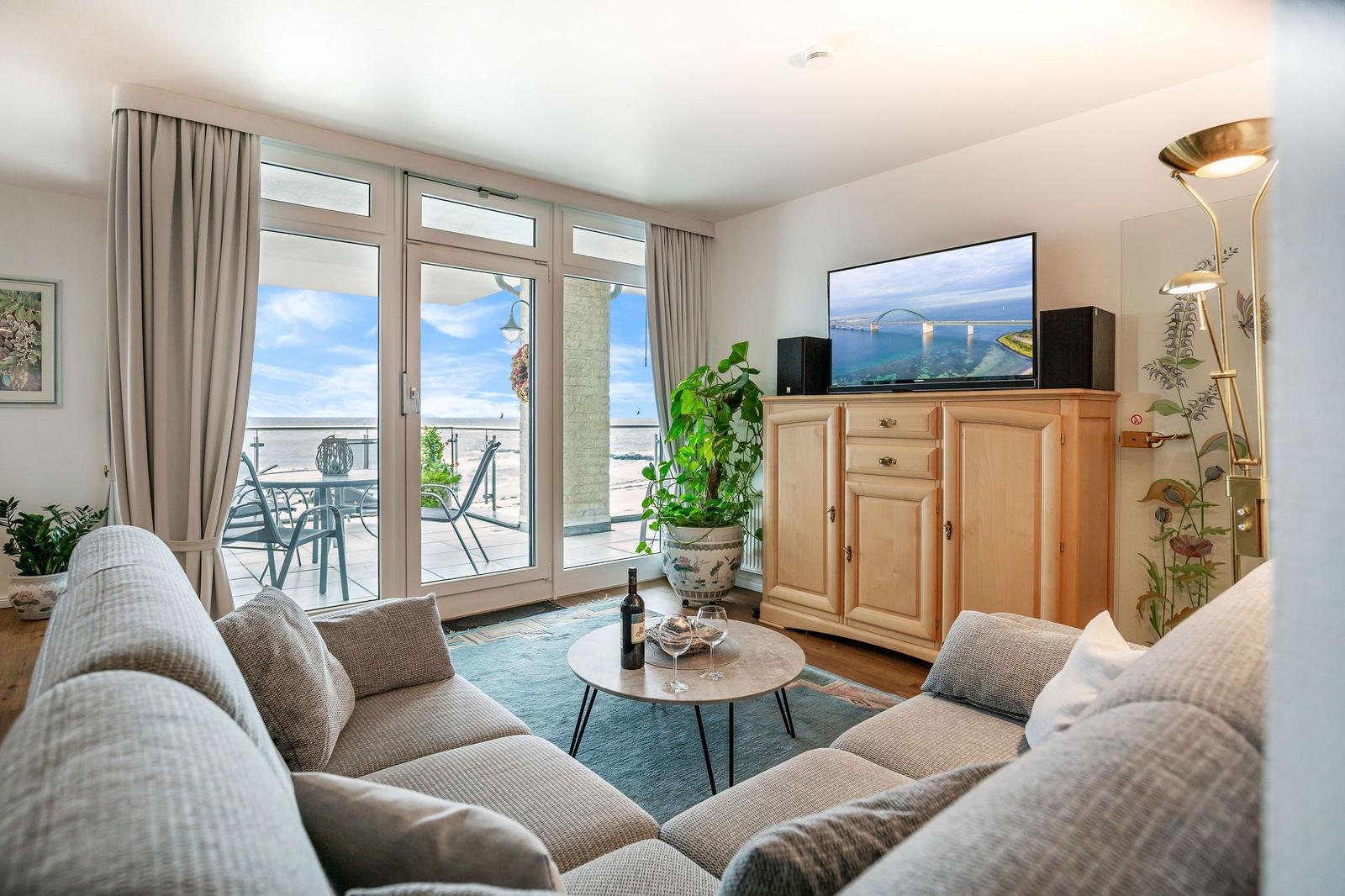 Wohnzimmer mit Sofa, TV und Balkonblick aufs Meer.