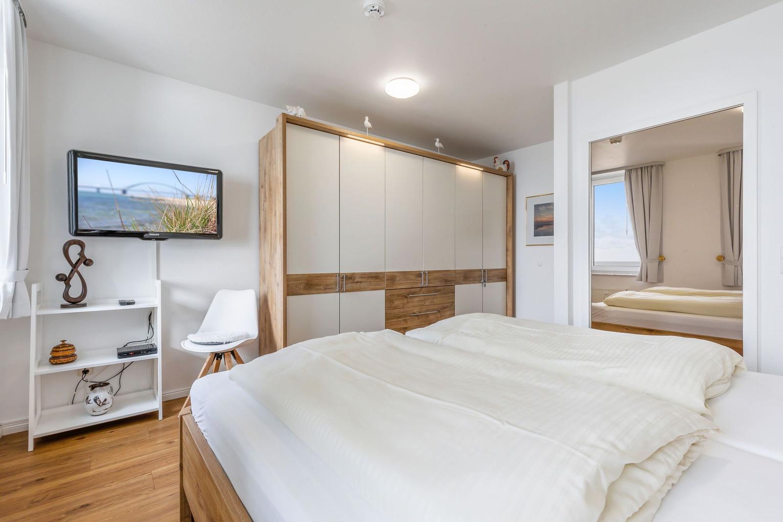 Schlafzimmer mit Doppelbett, Kleiderschrank und Fernseher an der Wand.