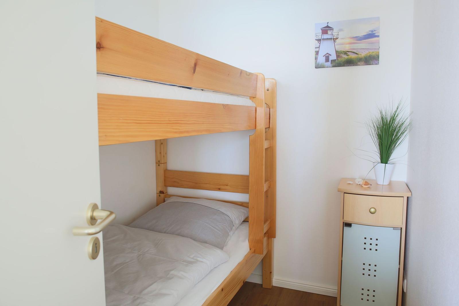 Doppelstockbett aus Holz, Nachttisch mit Pflanze und Leuchtturm-Bild an der Wand.