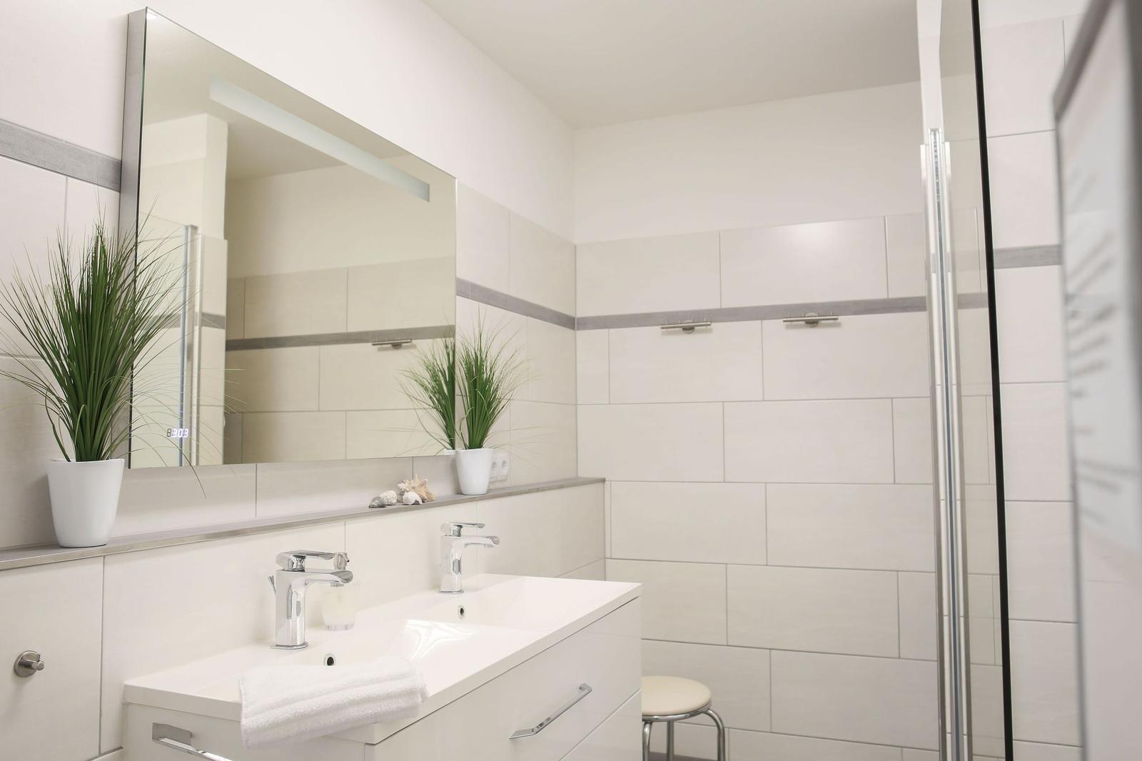 Badezimmer mit Dusche, Waschbecken und Spiegel.