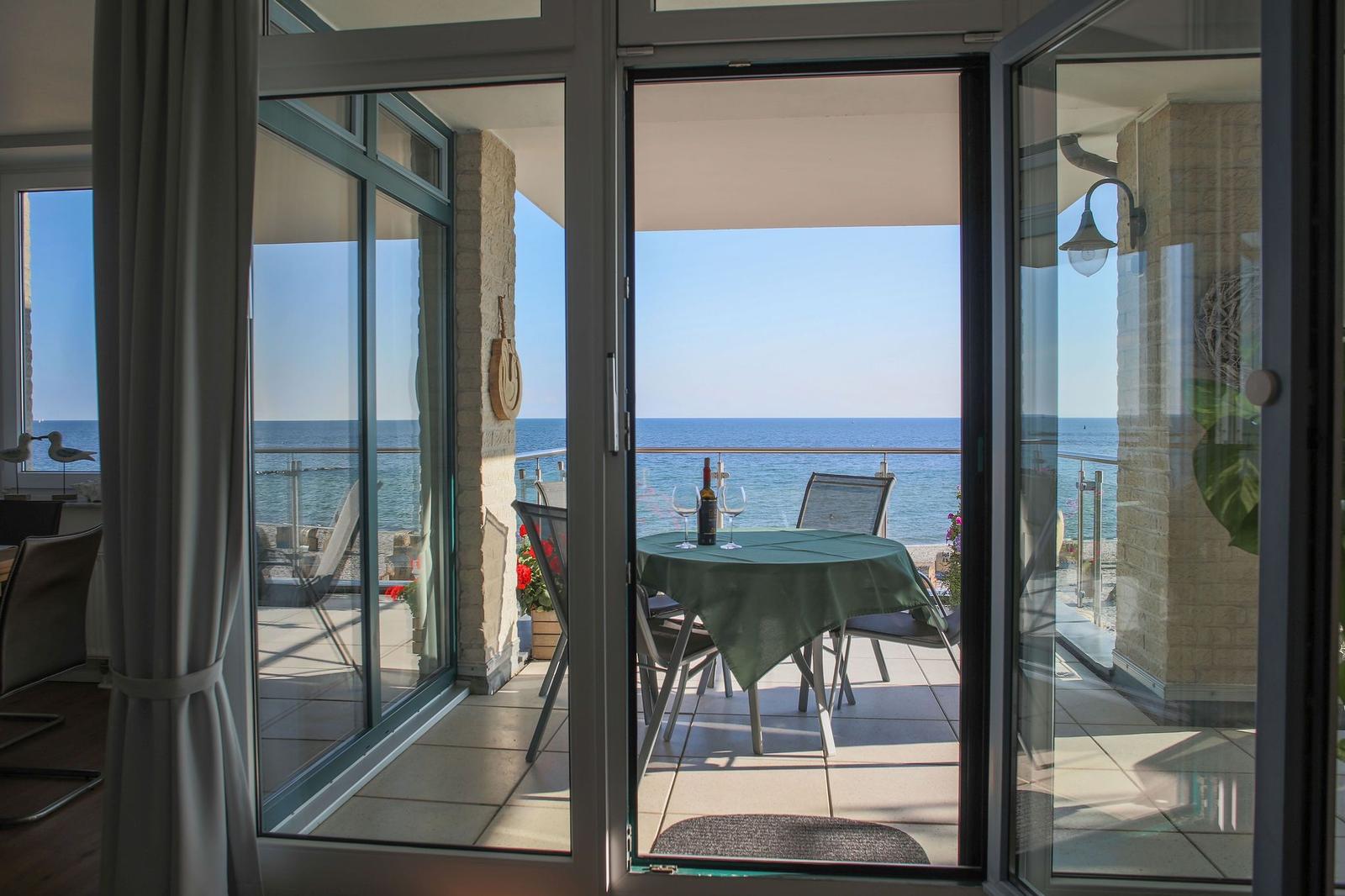 Terrasse mit Tisch und Stühlen bietet Meerblick. Glas-Türen führen vom Innenraum hinaus.