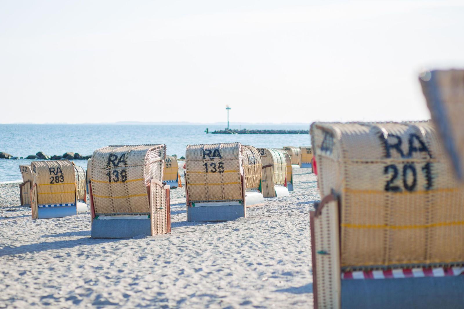 Strand mit Strandkörben, die auf Sand stehen und zum Meer blicken.