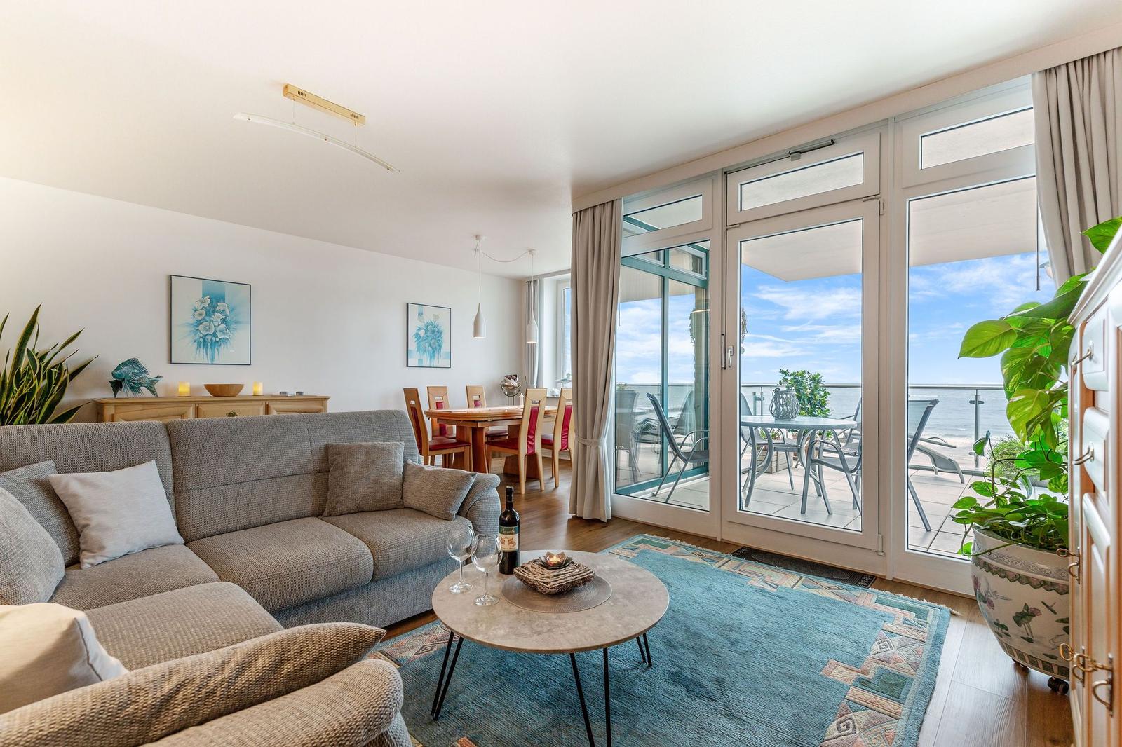 Wohnzimmer mit Sofa, Tisch und Blick auf Balkon mit Meerblick.
