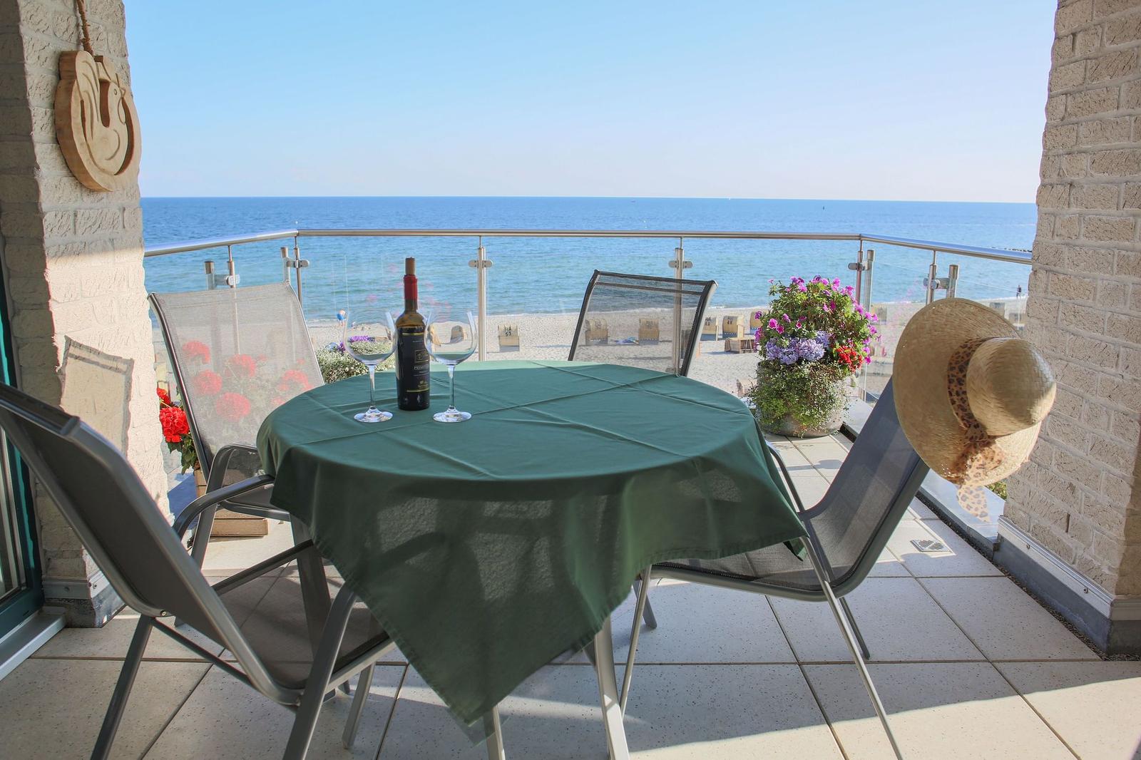 Terrasse mit Tisch, Stühlen und Meerblick. Ein Flasche Wein und zwei Gläser stehen bereit.