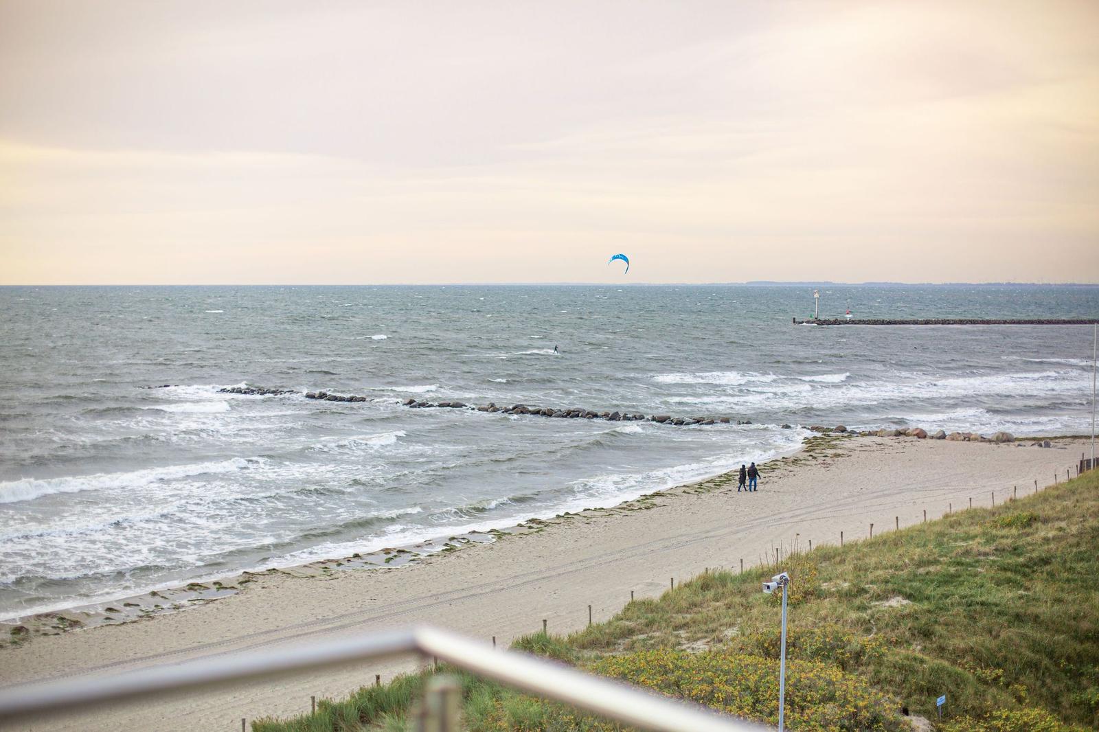 Meerstrand mit Kitesurfer und zwei Personen spazieren